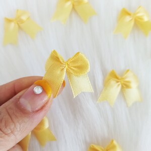 Peut inclure: Gros plan sur un nœud en satin jaune. Le nœud est tenu par un doigt avec un strass transparent sur l'ongle.