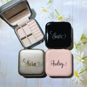 Pu&ograve; includere: Una collezione di portagioie personalizzati in nero, oro e rosa. Ogni custodia quadrata presenta un nome in elegante calligrafia: Susie, Sara e Audrey. Una custodia &egrave; aperta, rivelando scomparti.