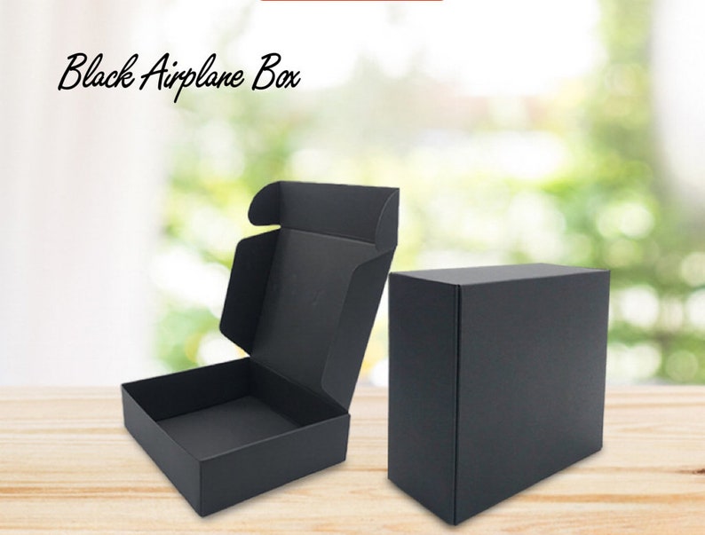May include: Two black cardboard boxes, one open and one closed. The boxes are on a wooden surface. The text "Black Airplane Box" is visible at the top of the image.