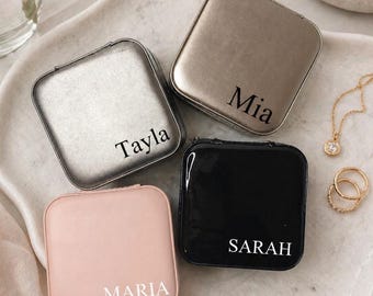 May include: Four personalized square compact cases in silver, gold, black, and pink. Each case has a name printed in white: Tayla, Mia, Sarah, and Maria. The cases are on a white tray with jewelry and a flower.