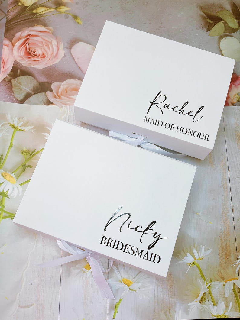 May include: Two white gift boxes with pink ribbon bows. The top box has the text "Rachel Maid of Honour" and the bottom box has the text "Nicky Bridesmaid".