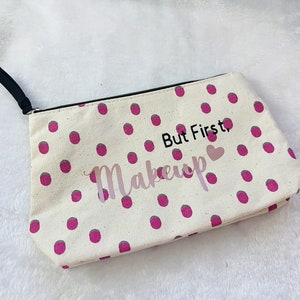 May include: A white canvas makeup bag with pink polka dots and the text "But First, Makeup" with a pink heart.