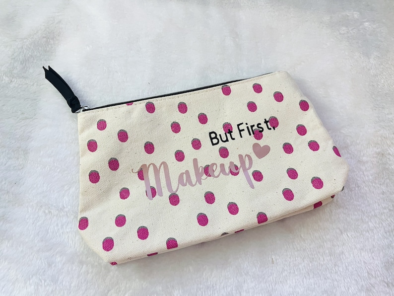 May include: A white canvas makeup bag with pink polka dots and the text "But First, Makeup" with a pink heart.