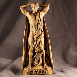 K&ouml;nnte beinhalten: Eine Holzskulptur des griechischen Gottes Apollon, der mit erhobenen Armen steht, eine flie&szlig;ende Robe tr&auml;gt und eine Leier h&auml;lt. Die Skulptur steht auf einem Sockel mit der Inschrift "APOLLO".