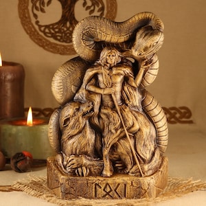 May include: A wooden statue of a Norse god, possibly Odin, with a wolf and a serpent. The statue is brown and gold in color and has intricate details. The base of the statue has the word "RAXI" carved into it.