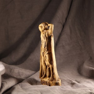 K&ouml;nnte beinhalten: Eine Holzskulptur eines Mannes in einem flie&szlig;enden Gewand, der mit erhobenen Armen &uuml;ber dem Kopf steht. Die Skulptur steht auf einem Sockel mit der Aufschrift "APOLLO".