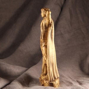 K&ouml;nnte beinhalten: Eine Holzskulptur einer Person, die eine lange Robe tr&auml;gt. Die Skulptur ist realistisch geschnitzt und hat eine warme braune Farbe.