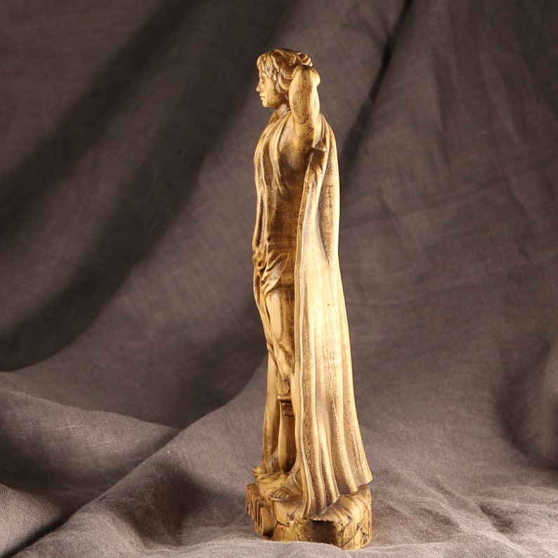 K&ouml;nnte beinhalten: Eine Holzskulptur einer Person, die eine lange Robe tr&auml;gt. Die Skulptur ist realistisch geschnitzt und hat eine warme braune Farbe.