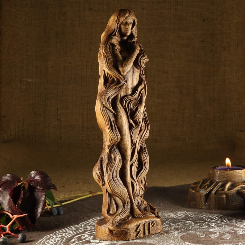 May include: A wooden sculpture of a woman with long flowing hair. The sculpture is carved in a detailed style and has a natural wood finish. The sculpture is standing on a base with the rune "Sig" carved into it.