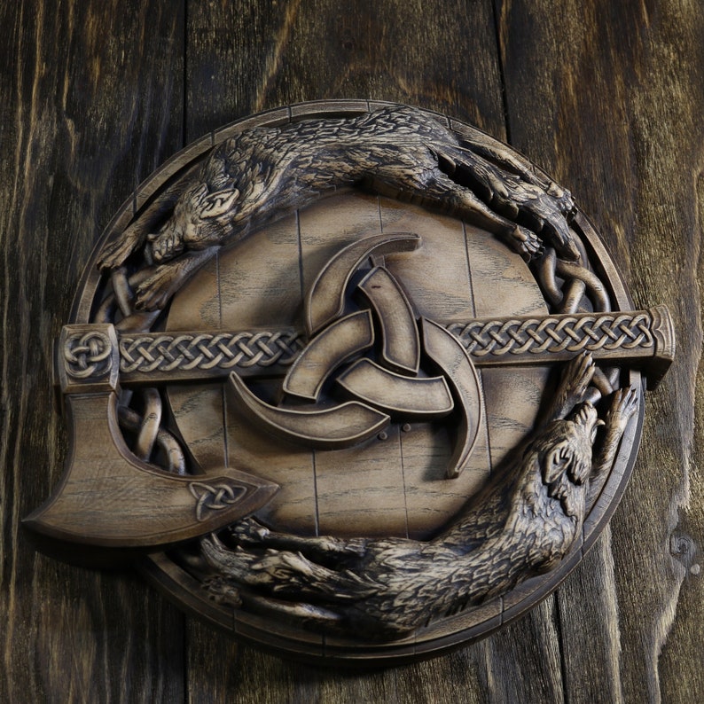 May include: A wooden wall plaque featuring a stylized depiction of a triquetra, a Celtic symbol of trinity, surrounded by two wolves. The wolves are carved in a realistic style and appear to be running in opposite directions. The plaque is made of dark wood and has a rustic finish.