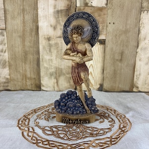 Peut inclure: Une figurine en bois de Morphée, le dieu grec des rêves, tenant un enfant endormi. La figurine est posée sur un socle orné de champignons et le nom "Morphée" y est inscrit.