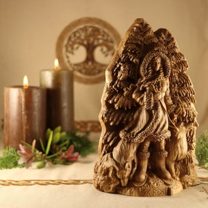 May include: A wooden carving of a woman standing in a forest with two dogs. The woman is wearing a long coat and a hood. The carving is detailed and intricate, with the woman's face and the dogs' fur clearly visible. The carving is made of a light brown wood and has a natural finish. The carving is signed "SKFN" at the bottom.