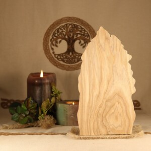 May include: A wooden cutout of a tree with a rough, natural texture. The cutout is standing on a burlap surface in front of a candle and a woven tree of life design.