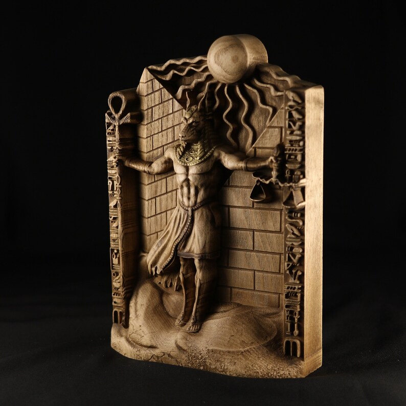 May include: A wooden sculpture of an Egyptian god with a jackal head, standing in front of a brick wall with hieroglyphs. The god is holding a staff in one hand and a scale in the other. The sculpture is carved in detail and has a realistic appearance.