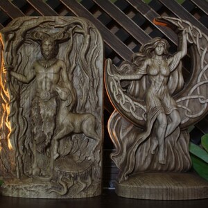 May include: Two wooden carvings of deities. The carving on the left depicts a male figure with antlers, standing in a forest setting. The carving on the right depicts a female figure standing on a crescent moon.
