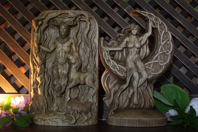 May include: Two wooden carvings of deities. The carving on the left depicts a male figure with antlers, standing in a forest setting. The carving on the right depicts a female figure standing on a crescent moon.