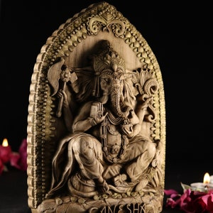 May include: A detailed wooden carving of the Hindu deity Ganesha, depicted with an elephant head, four arms, and a large belly. The carving is set against a background of intricate gold-colored designs.
