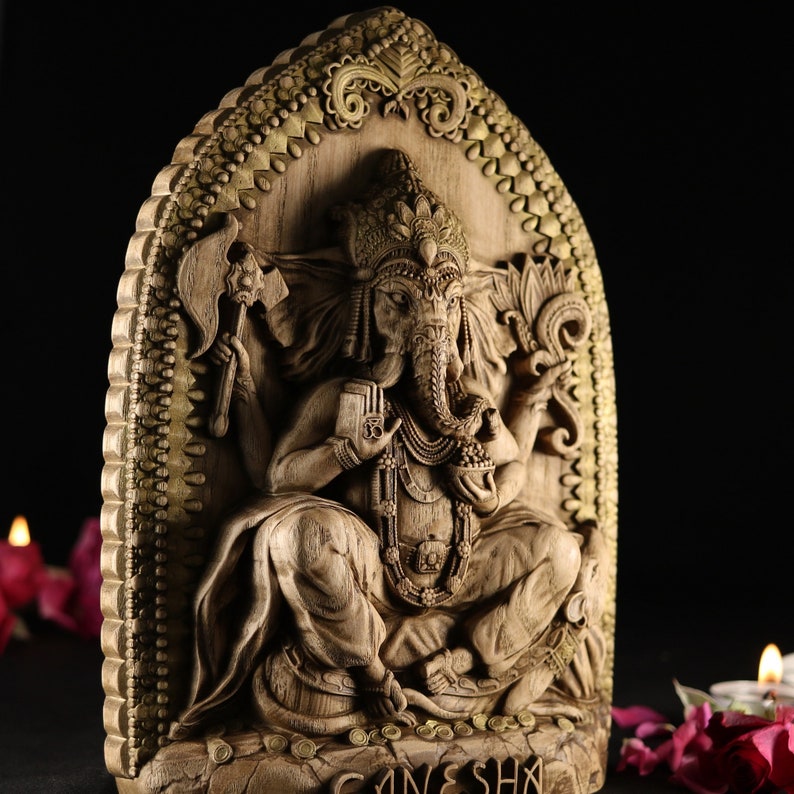 May include: A detailed wooden carving of the Hindu deity Ganesha, depicted with an elephant head, four arms, and a large belly. The carving is set against a background of intricate gold-colored designs.