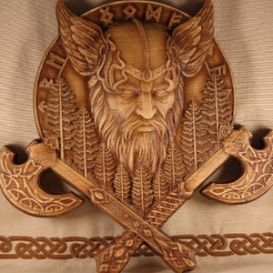 May include: A wooden wall hanging featuring a carved Viking warrior's head with a horned helmet, surrounded by a circle of runes and two crossed axes.