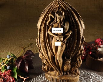 May include: A wooden statue of Lilith, a figure from Jewish mythology, depicted as a nude woman with horns and a skull in her hand. She is standing within a carved, flame-like structure. The base of the statue is inscribed with the word "Lilith".
