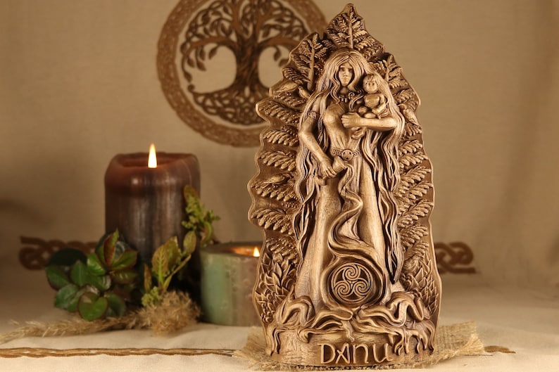 May include: A wooden carving of the Celtic goddess Danu, holding a child. The carving is detailed and features a Celtic knot design. The carving is on a wooden base with the name "Danu" inscribed on it.