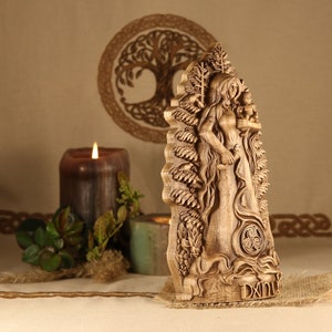 May include: A wooden carving of a Celtic goddess holding a child. The carving is detailed and intricate, with a tree of life design in the background. The carving is painted in a natural wood color and has a Celtic knot design at the bottom.