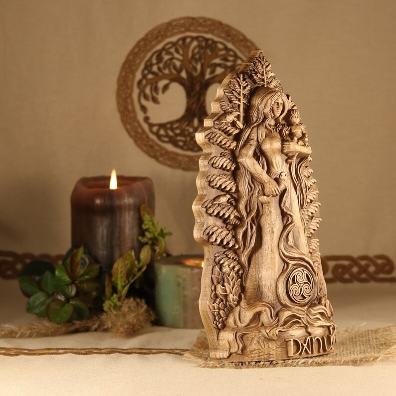 May include: A wooden carving of a Celtic goddess holding a child. The carving is detailed and intricate, with a tree of life design in the background. The carving is painted in a natural wood color and has a Celtic knot design at the bottom.