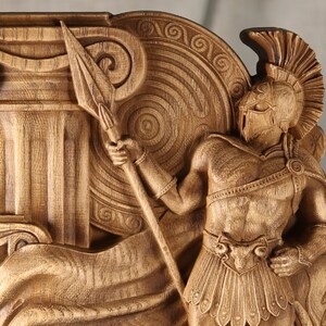Close-up view of a wooden Ares statue, showcasing the detailed high-relief carving of the Greek god's helmet, armor, spear tip, and fluted column.
