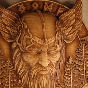 May include: A wooden carving of a Viking warrior with a beard and wings. The carving is detailed and intricate, with a focus on the warrior's face. The background is a wooden surface with a pattern of trees.