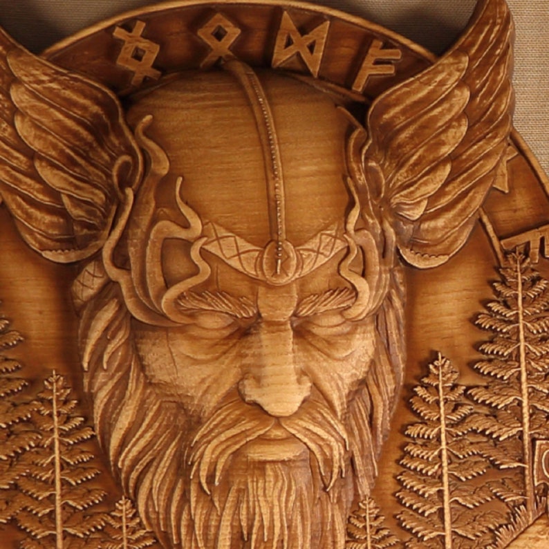 May include: A wooden carving of a Viking warrior with a beard and wings. The carving is detailed and intricate, with a focus on the warrior's face. The background is a wooden surface with a pattern of trees.