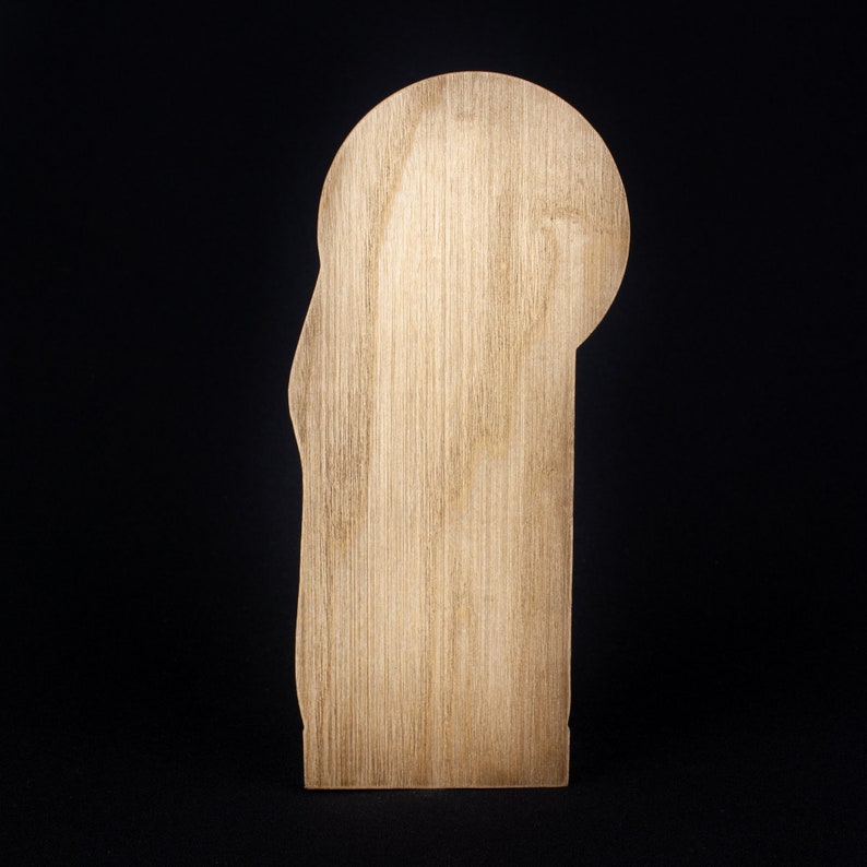 May include: A wooden cutout of a person's head and shoulders, with a rounded top and a flat bottom. The cutout is made of light brown wood with a natural grain pattern.