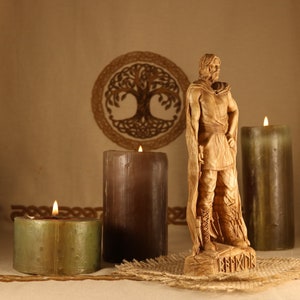 May include: A wooden carving of a Viking warrior standing on a base with the word "BEORNIX" inscribed. The warrior is wearing a cloak and holding a sword. The carving is surrounded by three candles, two brown and one green.