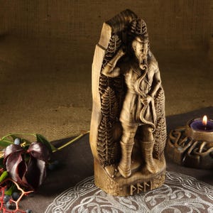 May include: A wooden carving of a Norse god, possibly Odin, holding a bow and arrow. The carving is detailed and features intricate designs. The carving is standing on a wooden base with the word "PFNN" inscribed on it.