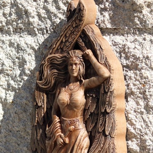 May include: A wooden carving of a woman with wings, her hair flowing behind her. The carving is detailed and intricate, with a focus on the woman's face and flowing hair.