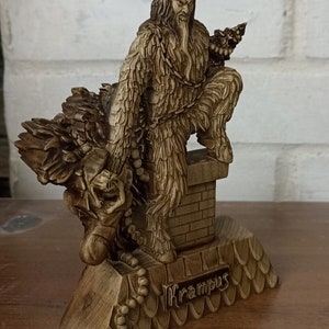May include: A detailed wooden Krampus figurine, featuring a horned, fur-covered creature with a chain, perched atop a chimney. The figurine is a light brown color and has intricate carvings. The word "Krampus" is inscribed on the base.