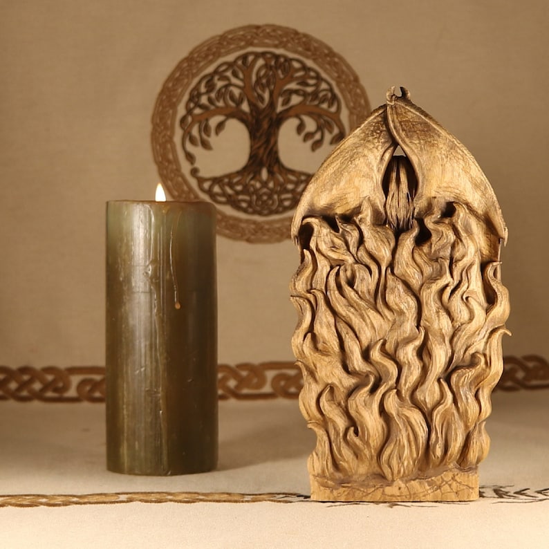 May include: A wooden sculpture of a figure with flames surrounding it. The sculpture is carved in a detailed style and has a warm brown color. The sculpture is sitting on a table with a candle in the background.