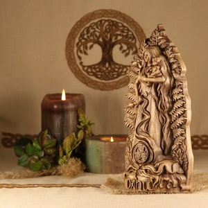 May include: A wooden carving of the Celtic goddess Danu, holding a child. The carving is detailed and intricate, with a Celtic knot design at the bottom. The carving is set against a backdrop of a wooden tree of life.