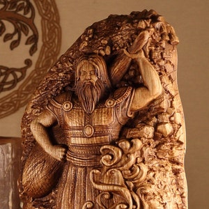 K&ouml;nnte beinhalten: Eine Holzschnitzerei eines nordischen Gottes, m&ouml;glicherweise Thor, der einen Hammer h&auml;lt. Die Schnitzerei ist detailliert und kunstvoll, mit einem strukturierten Hintergrund.