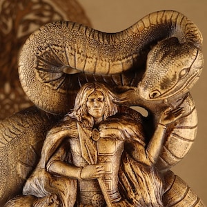May include: A wooden sculpture of a person with a snake wrapped around them. The person is wearing a cloak and has a serious expression on their face. The snake is brown and has a detailed texture.