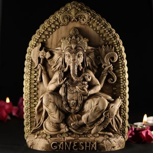 May include: A wooden sculpture of the Hindu deity Ganesha, carved in a detailed style. The sculpture depicts Ganesha sitting on a throne with his trunk raised and holding a sweet in his hand. The sculpture is painted in a warm brown color and has a gold-colored trim.