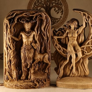 May include: Two wooden carvings depicting a horned god and a goddess. The god is standing in a forest scene, holding a staff and a deer. The goddess is sitting on a crescent moon, with her arms raised.