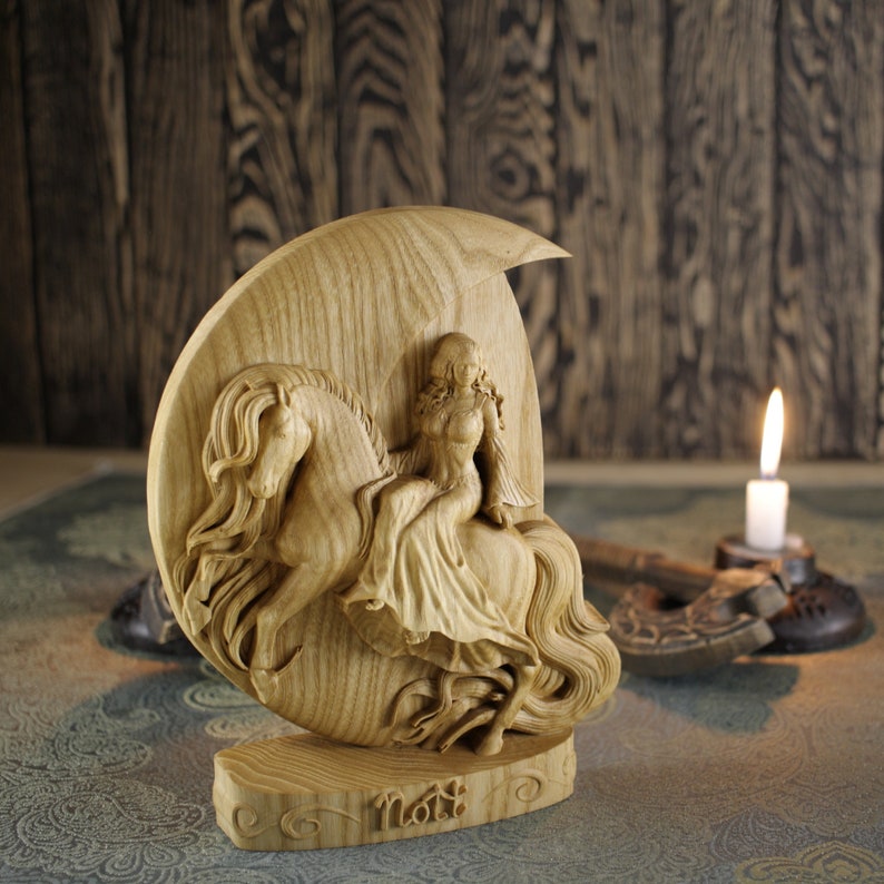 May include: A wooden sculpture of a woman riding a horse, with the woman's name "Noti" carved at the base. The sculpture is carved in a crescent moon shape.