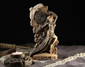 May include: A wooden figurine of the Celtic goddess Arianrhod, depicted as a woman in a flowing robe, standing on a base with her name inscribed. The figurine is surrounded by intricate carvings of Celtic knotwork and a triple spiral symbol.