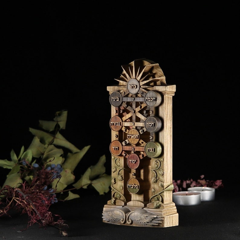 May include: A wooden sculpture of the Tree of Life, a Kabbalistic symbol, with Hebrew letters and a sunburst design at the top. The sculpture is carved in a light brown wood with details in darker shades of brown.