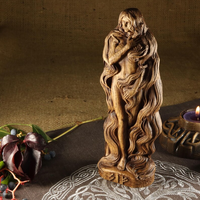 May include: Wooden statue of the Norse goddess Sif, depicted with long flowing hair and a serene expression. The statue is carved in a detailed style and stands on a base with the inscription "Sif".