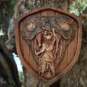 May include: A wooden shield with a carved image of a mythical creature with a large mouth and sharp teeth. A figure is depicted holding a lightning bolt and fighting the creature.