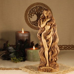 May include: A wooden sculpture of a woman with long flowing hair, standing on a base with the rune "Sig" carved into it. The sculpture is in front of a brown background with a Celtic knot design and two candles.
