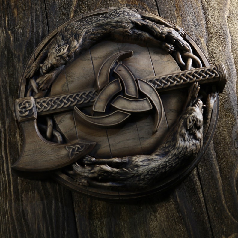 May include: A wooden wall plaque featuring a stylized depiction of a valknut, a Norse symbol of connection, with two wolves flanking the symbol. The plaque is carved in a dark wood and has a rustic, aged appearance.