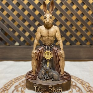 Op de afbeelding: Een houten beeld van een konijnen-godheid, Tu'er Shen, zittend met twee kleinere konijnen aan zijn voeten. Het beeld is geschilderd in tinten bruin en goud, en de godheid draagt een rood-gouden gewaad.