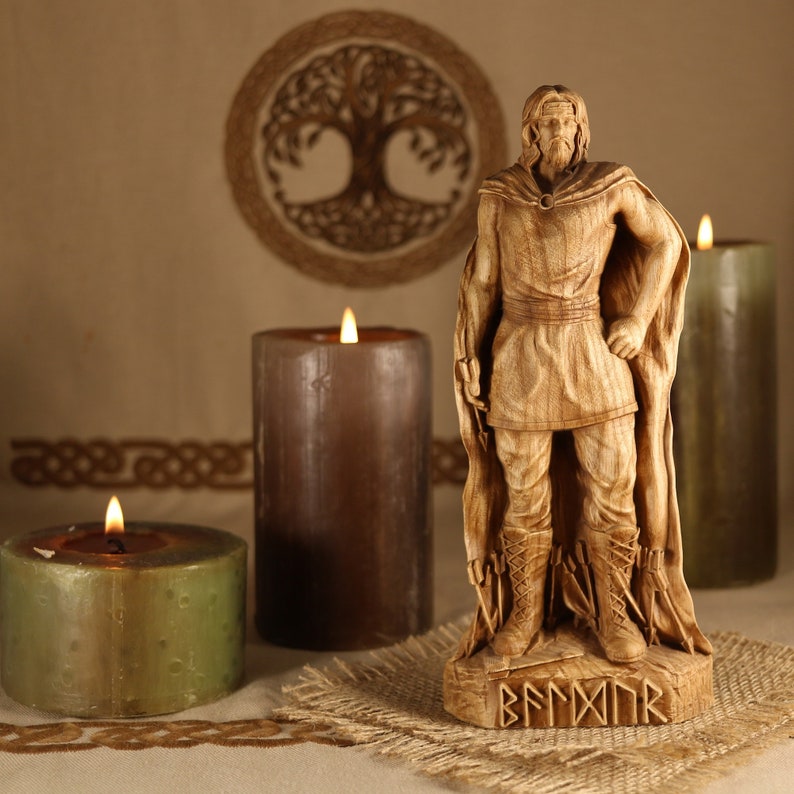 May include: A wooden statue of a Viking warrior with a beard and a cloak, standing on a wooden base with runes. The statue is surrounded by three candles, two brown and one green.
